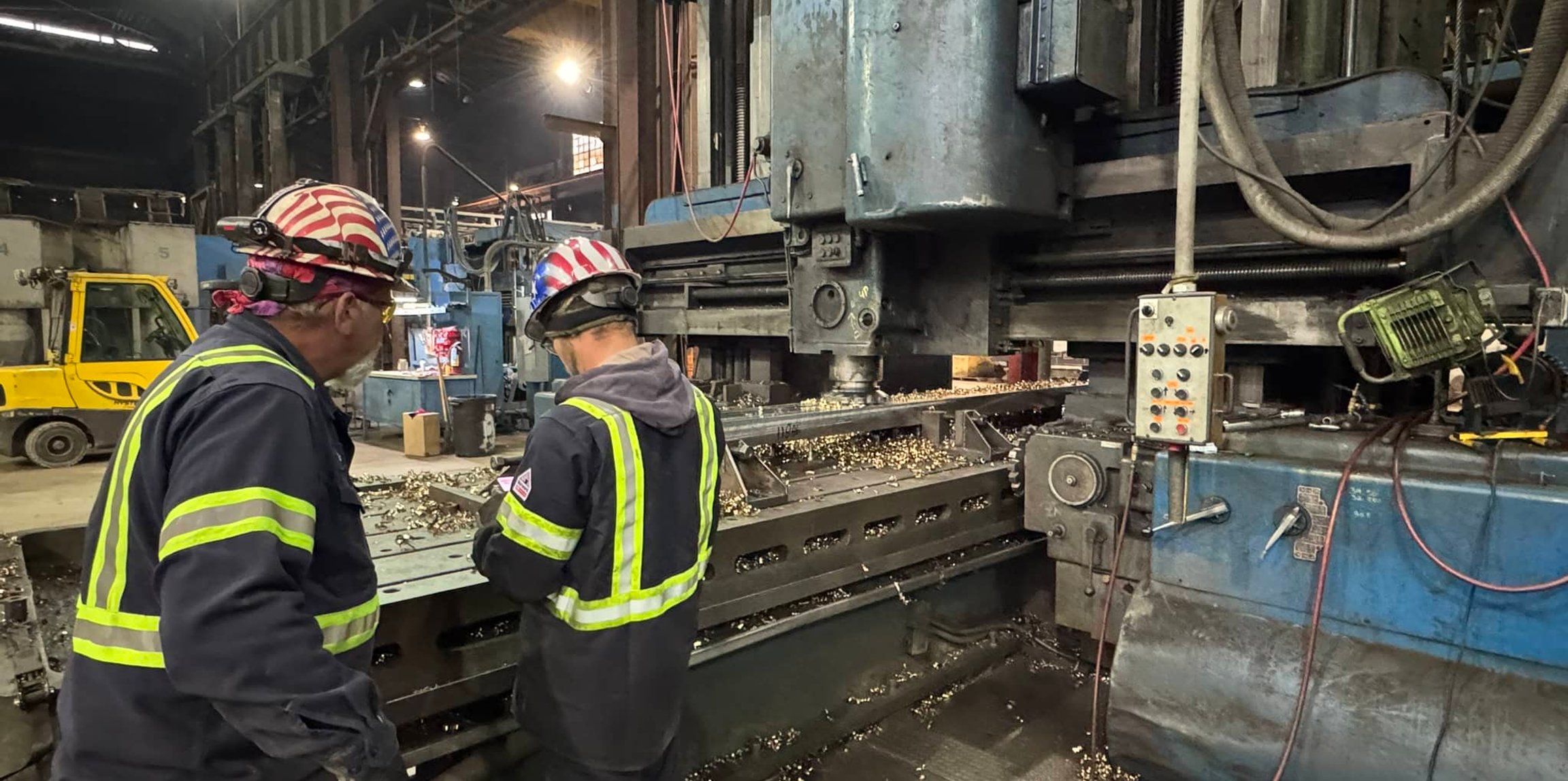 Two workers in hard hats operating a large industrial milling machine