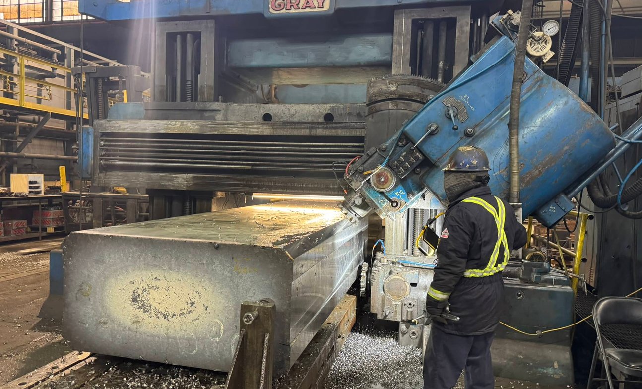 Two workers in safety gear inspecting a freshly machined steel shaft