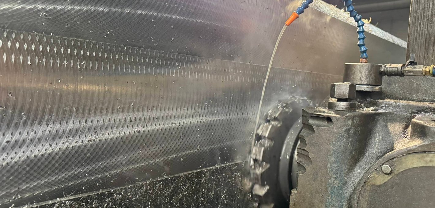 Close-up of textured steel cylinder being turned on a lathe with coolant