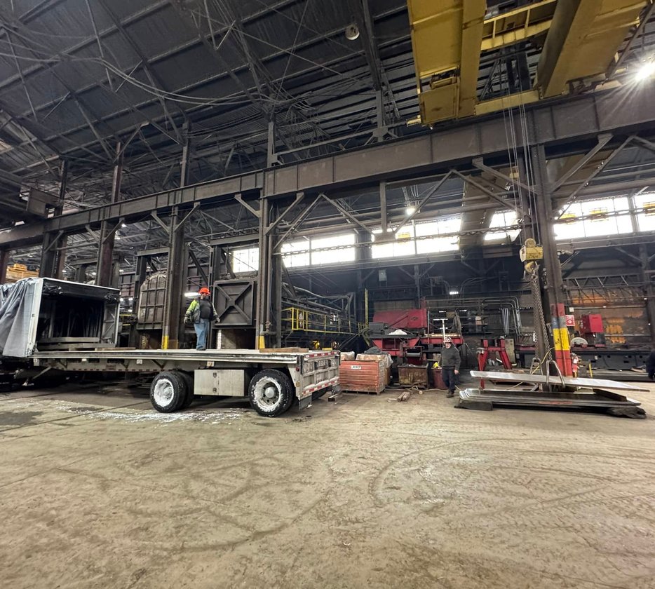 Worker adjusting coolant nozzle on a lathe turning a large steel cylinder