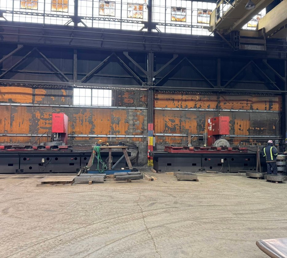 Worker adjusting coolant nozzle on a lathe turning a large steel cylinder