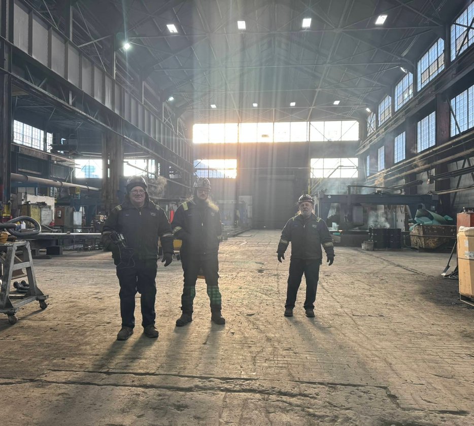 Worker adjusting coolant nozzle on a lathe turning a large steel cylinder
