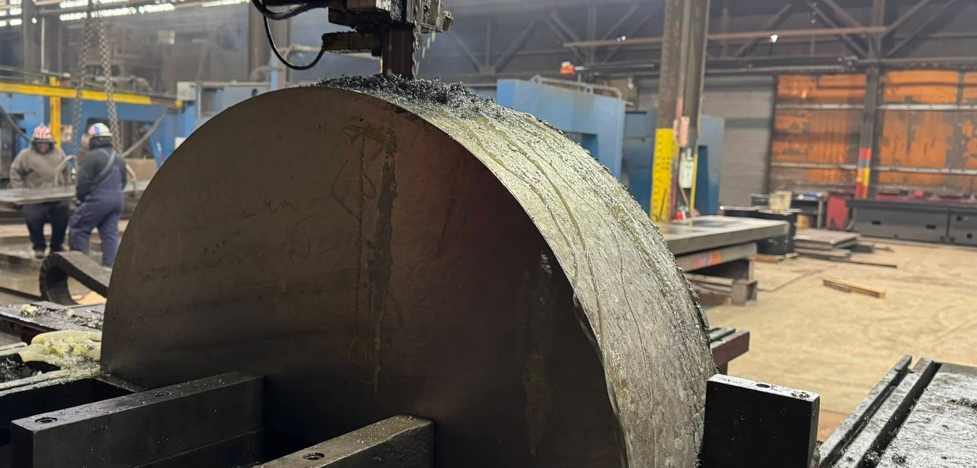 Large semicircular steel billet being cut by a bandsaw in industrial facility