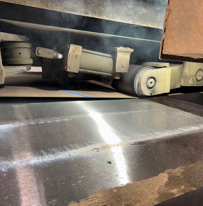 Close-up of a grinding wheel surfacing a polished steel plate with steam